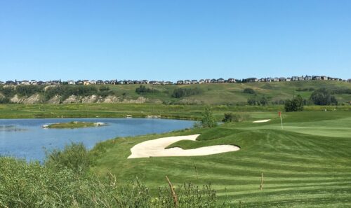 Photo of a golf course green and sand trap with pond in the background