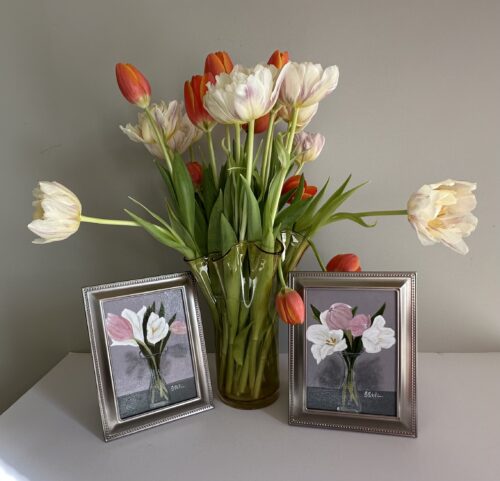 A small painting of pink and white tulips in a clear carafe