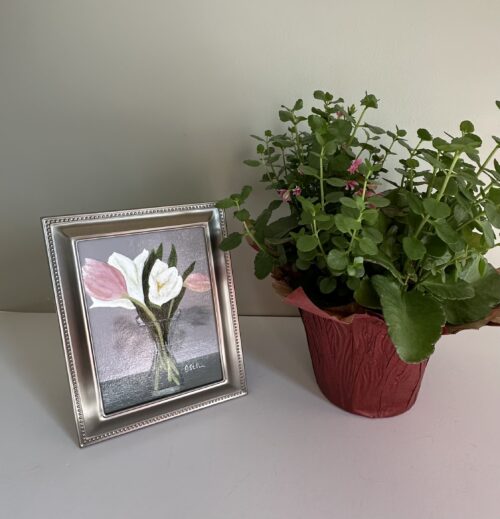 A small framed painting of pink and white tulips in a carafe