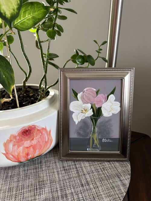 A small painting of pink and white tulips in a clear carafe