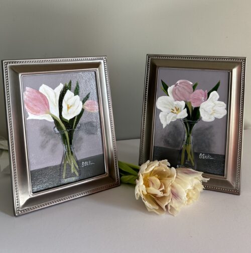 A small framed painting of pink and white tulips in a carafe