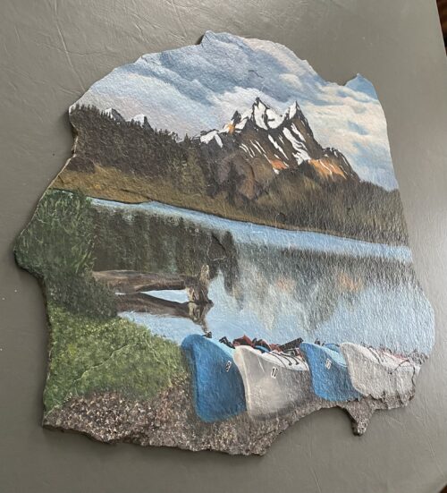 A photo of a large piece of slate stone, hand painted with a mountain and water scene