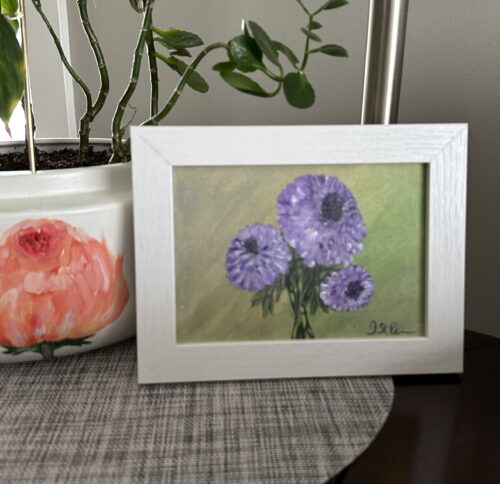 A painting of purple Chrysanthemums on a green background and in a white frame