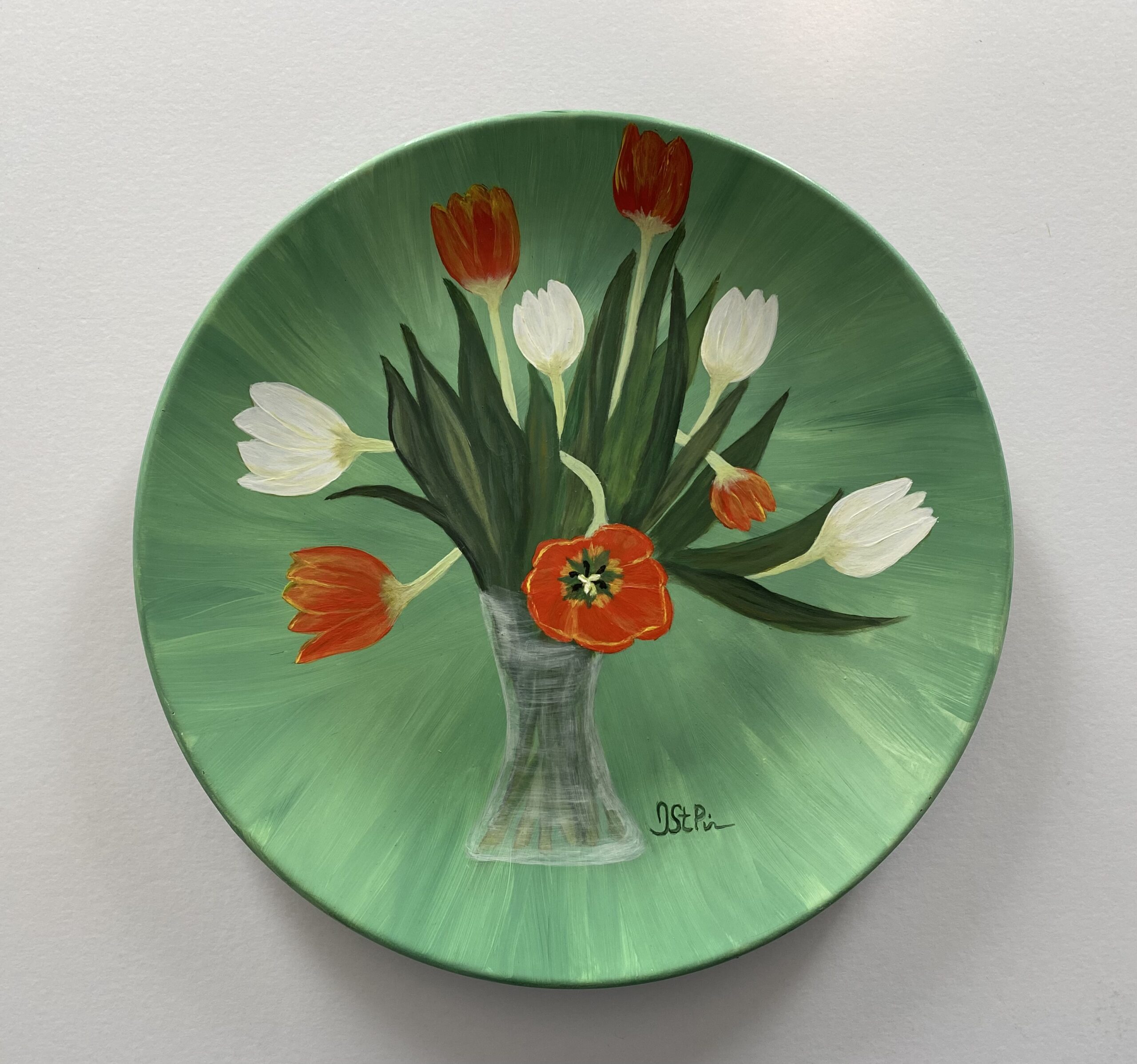 Photo of a green plate hand painted with orange and white twisting tulips in a glass vase